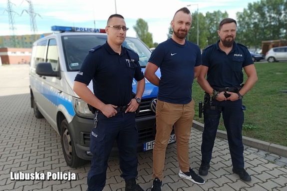 policjanci i mężcyzna stoją przed radiowozem