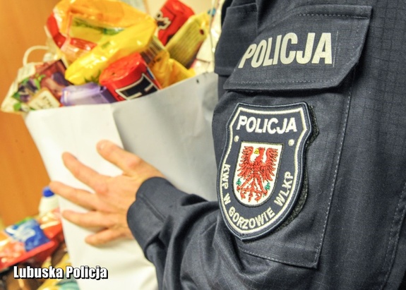 Policjant przy zbiórce produktów dla potrzebujących. Niesie torbę.