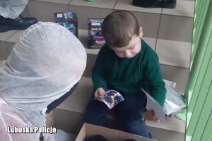 Policjant w specjalnym kombinezonie przekazują prezenty chłopczykowi
