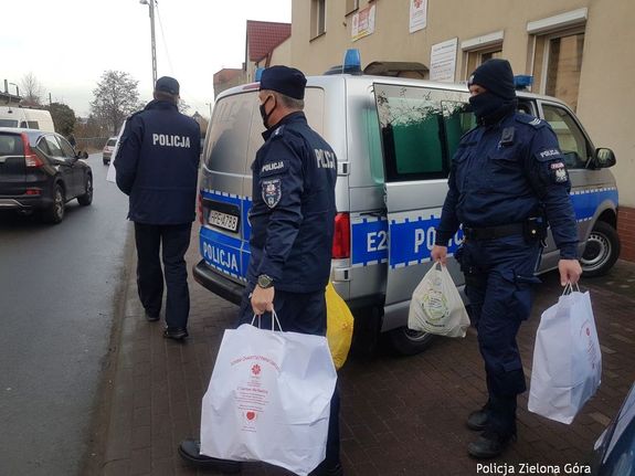 Policjanci z Komendy Miejskiej Policji w Zielonej Górze przy radiowozie pakują torby Caritas