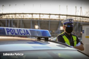 Policjant przy radiowozie. W tle gorzowski stadion żużlowy