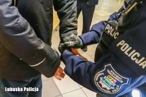Policjant nakłada kajdanki zatrzymanemu mężczyźnie.