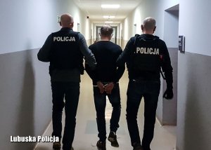 Nieumundurowani policjanci prowadzą zatrzymanego mężczyznę.