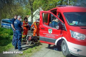 Policjanci i strażacy stojący przy pojeździe straży pożarnej.