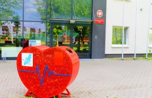 Pojemnik na nakrętki w kształcie serca. W tle budynek komendy Policji