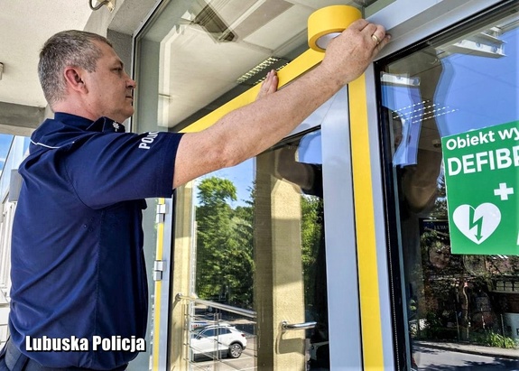 Policjant okleja taśmą drzwi wejściowe do komendy Policji.