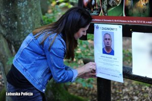 Kobieta umieszcza na tablicy ogłoszeniowej foto komunikat o zaginionym.