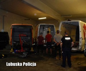 Policjant z zatrzymanymi osobami w garażu, w którym znajdują się skradzione mercedesy