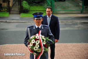 Policjant składający wieniec. W tle mężczyzna