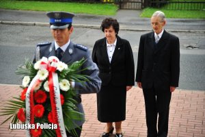 Policjant składający wieniec. W tle małżeństwo- rodzina Alojzego Banacha