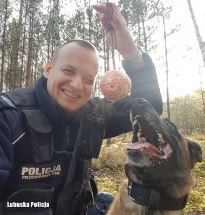 Policjant, a obok niego policyjny pies patrzący na piłkę.