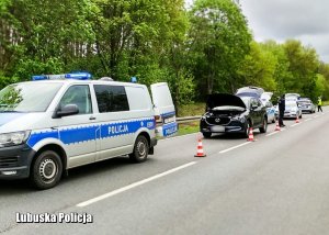 Policyjny bus, a za nim zatrzymany do kontroli drogowej pojazd. Obok policjanci.