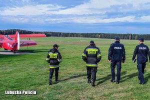 Policjanci i strażacy na lotnisku - w tle samolot.