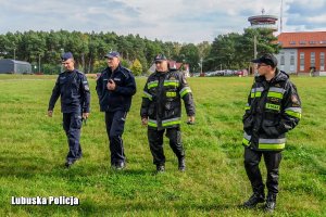 Policjanci i strażacy na lotnisku - w tle budynek.