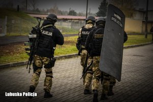 policjanci idą z długą bronią i tarczą