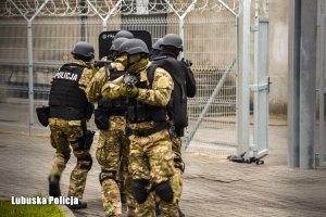 policjanci z długą bronią i tarczą idą w kierunku budynku