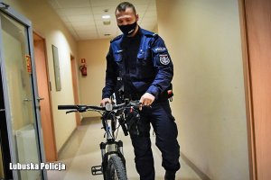 policjant idzie korytarzem z odzyskanym rowerem