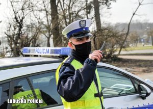 Policjant drogówki w maseczce radiowej trzyma w dłoni radiostację.