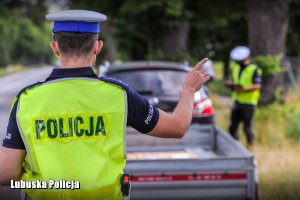 Policjant drogówki sprawdza oświetlenie pojazdu zatrzymanego do kontroli drogowej.