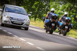 Policyjne motocykle jadące obok pojazdu.