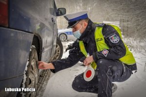 Policjant drogówki sprawdzający stan opon w pojeździe.