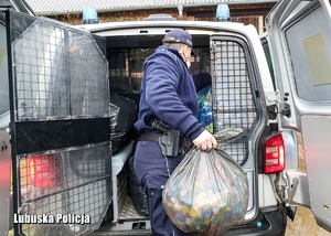 Policjant wyciąga worek nakrętek z radiowozu.