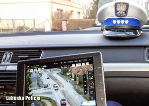 Wyświetlacz kontrolera drona, a w tle czapka policjanta drogówki we wnętrzu radiowozu.