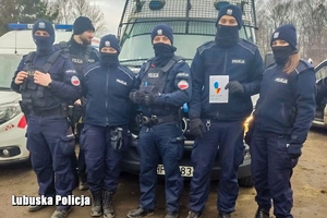 Policjanci oddziałów prewencji stojący przy radiowozie.