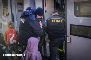 Policjant i strażak pomaga wejść do pociągu rodzinie uchodźców.