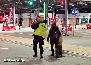 Policjant pomaga w niesieniu walizek uchodźców.