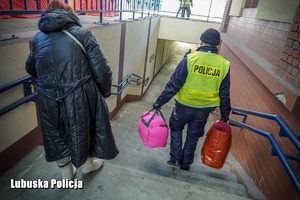 Policjant pomaga kobiecie nieść bagaże po schodach.