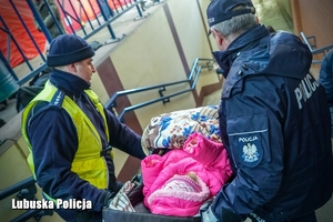 Policjanci niosą wózek z dzieckiem po schodach.