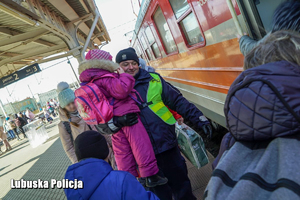 Policjant niosący dziecko na peronie kolejowym.