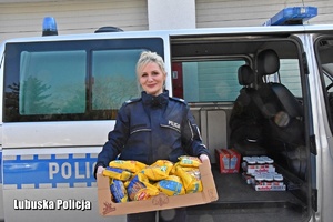 Policjantka trzyma karton z darami na tle radiowozu