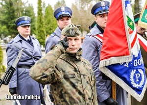 Żołnierz oddający hołd, a w tle policjanci pocztu sztandarowego.