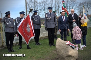 policjanci oddają honor w kierunku pomnika i posadzonego dębu