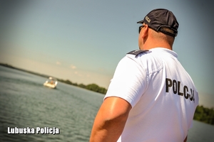 Policjant spogląda na łódź płynącą jeziorem.