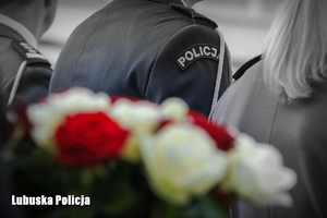 Zdjęcie policjantów, a na pierwszym planie wiązanka biało - czerwonych kwiatów.