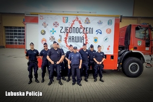 Policjanci na tle wozu strażackiego z plakatem akcji krwiodawstwa