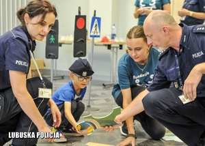 chłopiec z policjantami i przedstawicielka fundacji układają edukacyjne puzzle