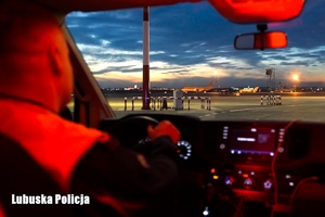 Policjant jadący radiowozem po płycie lotniska.