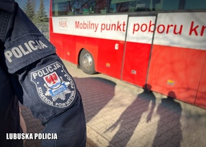 Policjant stojący na tle krwiobusa.