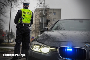 Policjant drogówki stojący przy nieoznakowanym radiowozie.