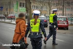 Policjanci przeprowadzają starszą kobietę przez jezdnię