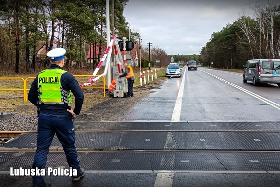 Policjant na przejeździe kolejowym przy uszkodzonych przez kierowcę rogatkach