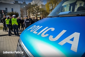 radiowóz i policjanci rozmawiający z uczniami klasy mundurowej w tle