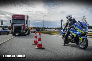 Policyjny motocyklista zatrzymuje do kontroli pojazd ciężarowy.