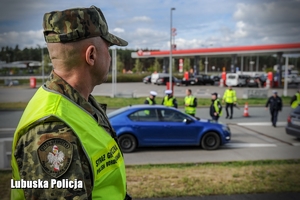 Funkcjonariusz Straży Granicznej, a w tle policjanci podczas kontroli.