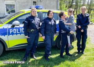 Kobieta z dzieckiem oraz policjantki stojące przy radiowozie.