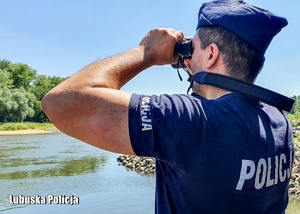 Policjant patrzy przez lornetkę nad rzeką.